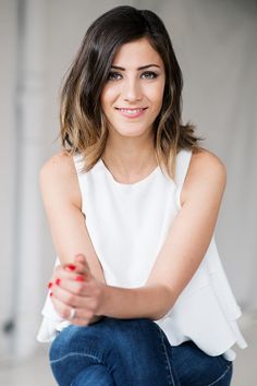 a woman sitting on the ground with her legs crossed and smiling at the camera,