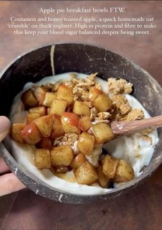 someone is holding a spoon over a bowl of food with yogurt and apples