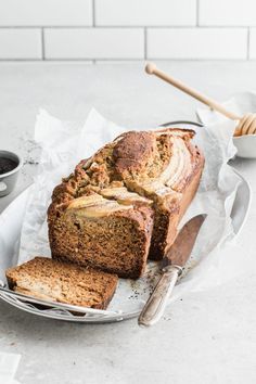 a loaf of banana bread on a plate with two slices cut from it and some coffee in the background