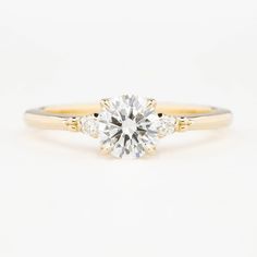 a yellow gold engagement ring with two diamonds on the band and a round brilliant cut diamond in the center