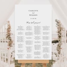 a wooden easer with a seating chart on it in front of an outdoor ceremony