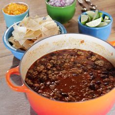 a pot filled with chili and chips on top of a wooden table next to other bowls