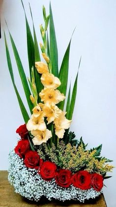 a vase filled with flowers and greenery on top of a wooden table in front of a white wall