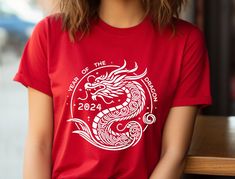 "Unleash Your Inner Dragon in 2024 with this stylish unisex Tee!  Rise to the occasion in this fierce Year of the Dragon t-shirt, featuring a bold and vibrant design that celebrates the power and majesty of this mythical creature. Made with Airlume combed and ring-spun cotton, this tee is incredibly soft and breathable, perfect for both active wear and leisure.  Here's why you'll love it:  * Classic unisex jersey short sleeve tee: This timeless design flatters everyone and pairs perfectly with j New Year Red T-shirt With Graphic Print, Red Graphic Print T-shirt For New Year, New Year Graphic Print Short Sleeve T-shirt, Dragon Shirt, Mythical Creature, Heather Green, Year Of The Dragon, Tai Chi, Vibrant Design