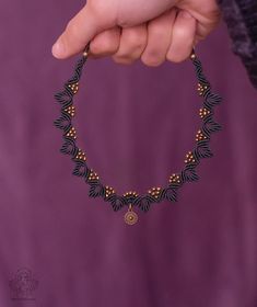 a person holding onto a black and gold beaded bracelet with small leaves on it