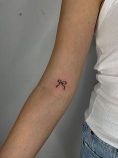 a woman's arm with a small bow tattoo on the left side of her arm