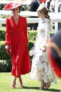 two women in red dresses and hats are standing next to each other on the grass