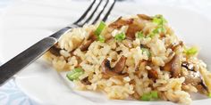 a white plate topped with rice covered in mushrooms and green onions next to a fork