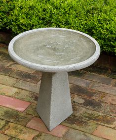 a concrete bird bath sitting on top of a brick walkway