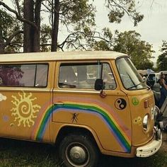 an old yellow van painted with sun and rainbows is parked on the grass in front of some trees