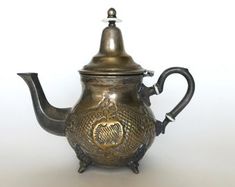 an ornate teapot with a lid and handle on a white background, it appears to be made of metal