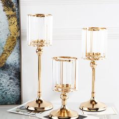 three gold candlesticks with clear glass shades on them sitting on top of a table