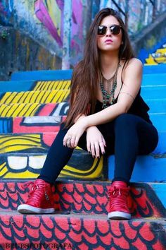 a woman sitting on some steps with her legs crossed and wearing red shoes in front of graffiti