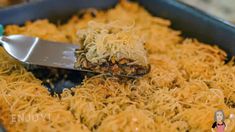 a spoon with some food in it on top of a pan filled with noodles and grated cheese