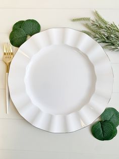 a white plate with green leaves and a gold fork on the side next to it