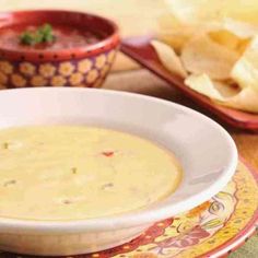 a bowl of soup on a plate with chips and salsa in the backgroud