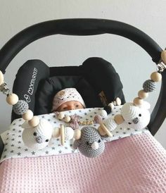 a baby in a car seat wearing a knitted hat and pacifier necklaces