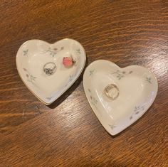 two heart shaped dishes with wedding rings on them sitting on top of a wooden table