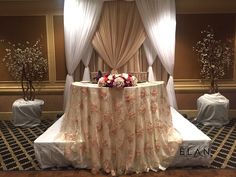 the table is covered with white draping and floral centerpieces on it