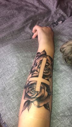 a woman's arm with a cross and rose tattoo on the side of it