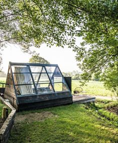 a house made out of windows sitting in the middle of a lush green field next to a tree