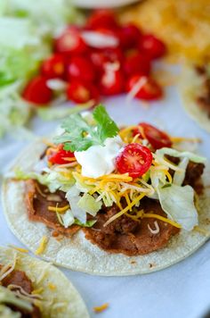 two tacos with meat, lettuce and tomatoes on them sitting on a table