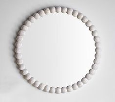 a round mirror mounted on the wall above a white beaded bracelet that is hanging from a hook