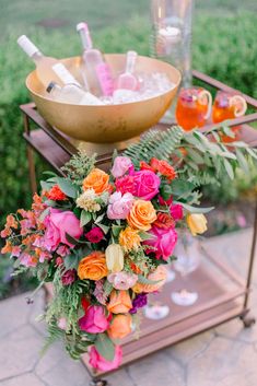 a bar cart with flowers and bottles on the top is decorated with greenery, candles and wine glasses