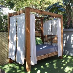 an outdoor bed with curtains on it in the grass next to a fence and trees