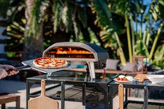 two people are cooking pizzas on an outdoor grill