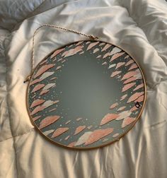 a round mirror with pink and grey designs on it sitting on a white bed sheet