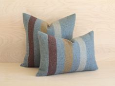 two blue and brown striped pillows sitting on top of a wooden table next to each other