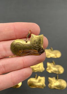 a hand holding a small gold cat charm in it's left hand and several smaller gold cats on the other side