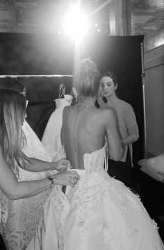 a woman in a wedding dress is helping another woman put on her dress while others look on