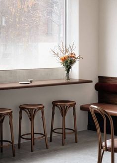 three wooden stools in front of a window with flowers on the table and bench