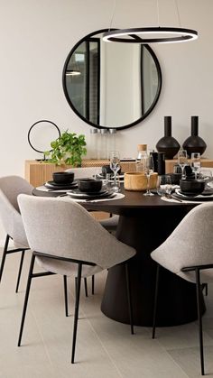 a dining room table with chairs and a round mirror on the wall above it,