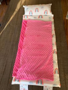 a pink blanket laying on top of a wooden floor next to a pillow and pillows