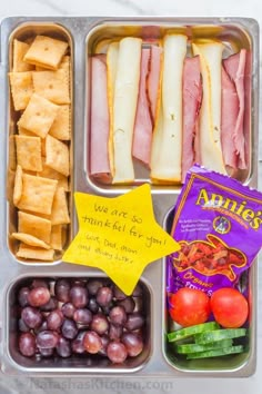 an open lunch box with ham, grapes, crackers, and other food items