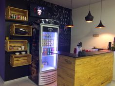 a small refrigerator with drinks inside of it in a room filled with shelves and hanging lights