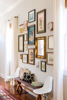 a wall filled with lots of framed pictures next to a wooden bench on top of a hard wood floor