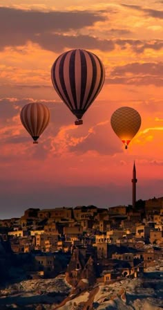 three hot air balloons flying over a city at sunset