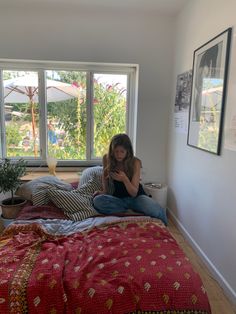 a woman sitting on top of a bed next to a window with lots of windows