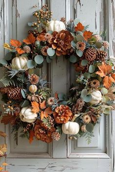 a wreath with pumpkins and leaves hanging on the front door to decorate for fall