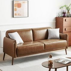 a brown leather couch sitting in a living room next to a coffee table and dresser