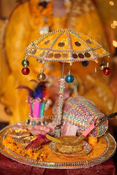 an elaborately decorated tray with beads and decorations on it's sides is displayed in front of a gold statue