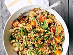 a white bowl filled with rice and vegetables on top of a wooden table next to a fork