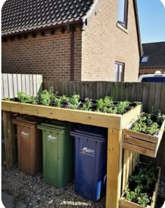 a wooden planter filled with lots of plants next to a fence and building in the background