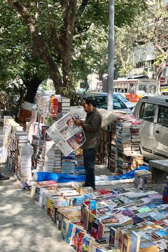 a man standing on the side of a road next to a pile of books