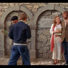 two men and a woman standing in front of a stone wall