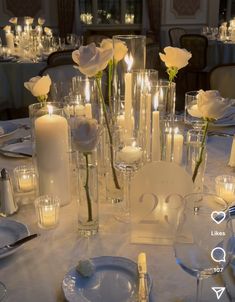 the table is set with candles, plates and vases filled with white rose flowers